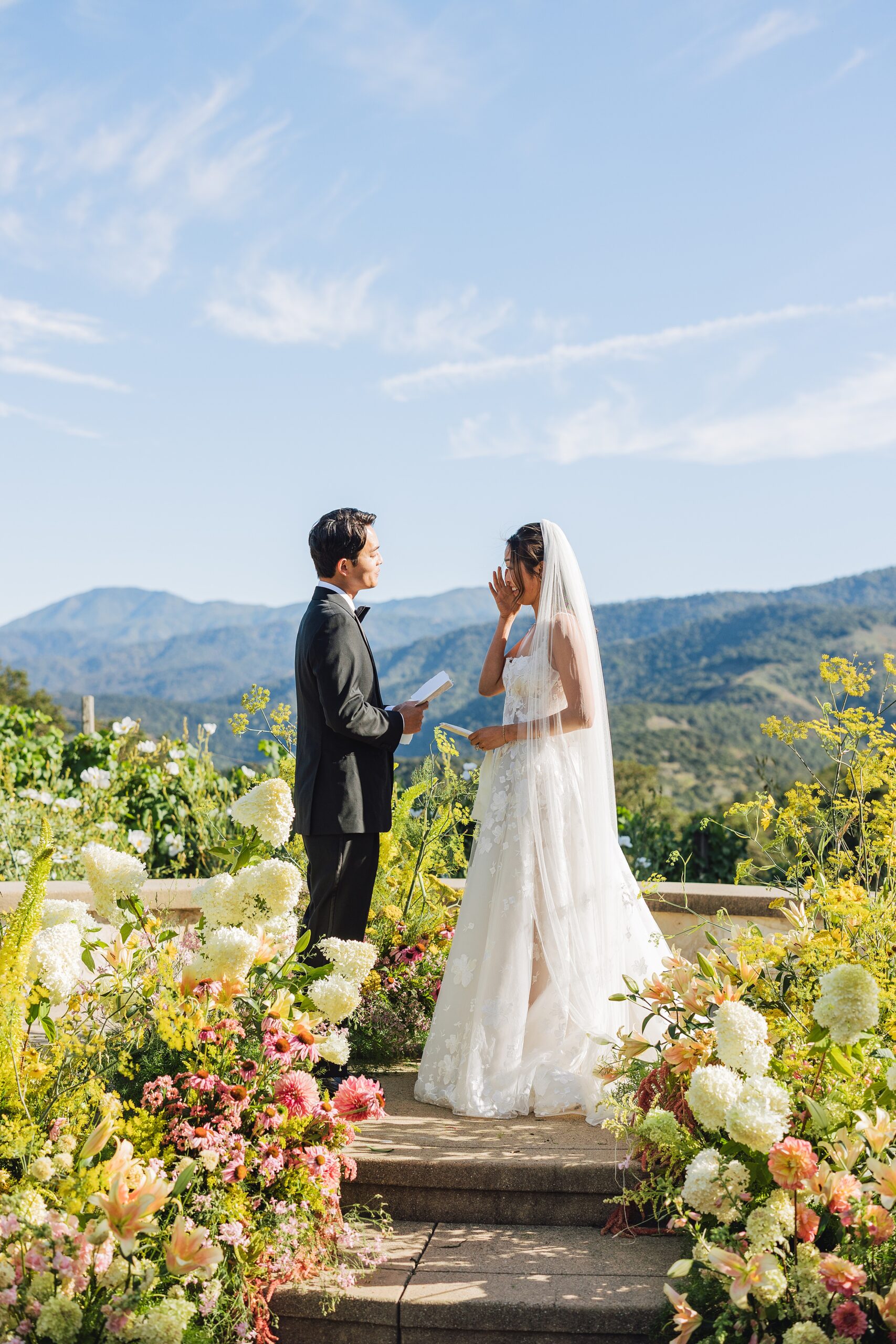 Bride wiping tears during wedding vows at Holman Ranch in Carmel Valley, surrounded by organic garden-inspired florals and vineyard backdrop