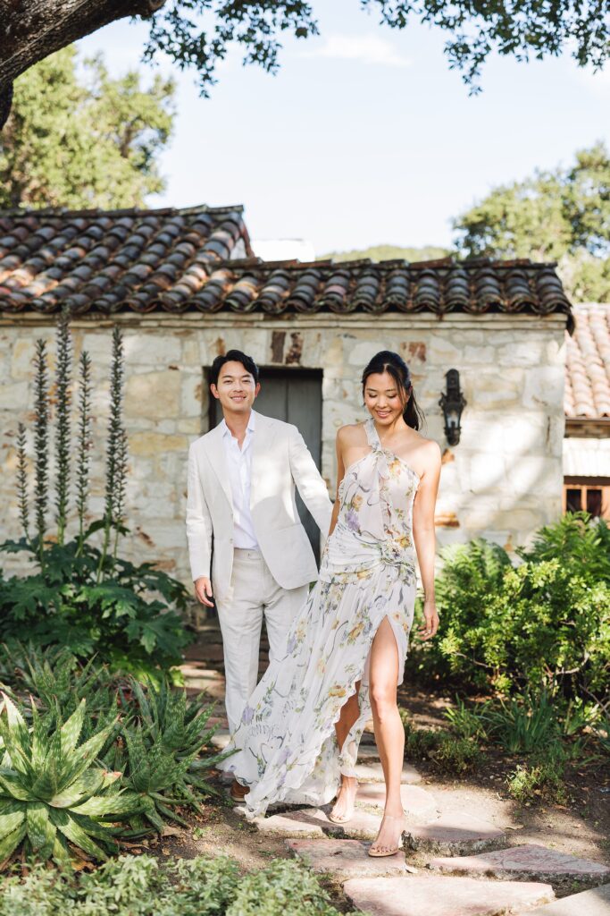 Bride and groom wedding welcome dinner portrait in front of historic stone building at Holman Ranch, Carmel Valley, bride holding romantic floral bouquet.